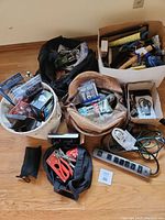 Photo showing overall lot including soft bags and box containing various tools and hardware items like hand tools, cords, extension strip, measuring tape, and small tool kits.