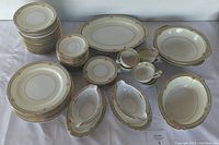 Full set of Noritake Lynbrook china arranged showing variety of plates, bowls, platters, and gravy boats with floral and gold trim pattern.