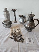 Group photo showing two teapots, shaker, vase, and ornate forks with bag on white cloth