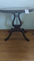 Front view of oval wooden vintage side table with harp motif on pedestal base, scratches visible on surface and legs.