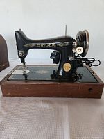 Side profile of black Singer sewing machine mounted on wooden base showing gold detailing.