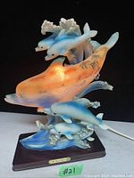 Front view of vintage dolphin table lamp with glowing effect inside large dolphin, showing three smaller blue dolphins and ocean wave base.