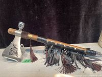 Full side view of the peace pipe tomahawk showing wooden handle with leather decorations and metal blade with engraving.