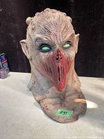 Front view of detailed horror monster mask with textured skin, glowing green eyes, and red mouth area.