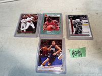Four sports cards displayed on a table: baseball card of Vladimir Guerrero, basketball card of Michael Jordan, hockey card of Curtis Joseph, and basketball card of Steve Nash. Each card is shown in a clear protective sleeve.