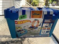 Photo of sealed blue storage box with white straps, showing Hot Wheels logo and Track Builder graphics, illustrating multi loop track design and launcher.