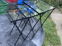 Set of three black iron nesting tables with glass inset tops displayed on patio table. Showing smallest to largest size.