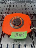 Photo showing the rectangular orange plastic case of the Lufkin measuring tape, model HV/30CME, with a black circular dial on the front and a metal keyring attachment.