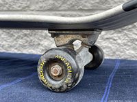 Close-up image of black Barracuda branded wheel showing wear on surface and aged metal truck attached to aluminum deck.