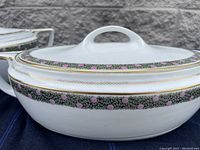 Close-up photo of the lid showing the decorative pink rosebuds and green leaf pattern with gold trimmed edges.