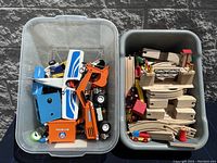 Two bins containing wooden train tracks, various toy vehicles including a helicopter, and an orange Polar-Lab labeled plastic box.
