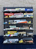 Full view of the die-cut trailer trucks displayed on a black shelf unit outside on a stone wall background.
