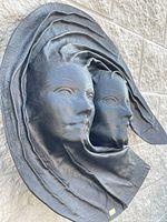 Front view showing two human faces emerging from molded leather with flowing folds, round shape approx. 24 inches.