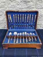 Full view of the wooden cutlery display case showing inlaid silver plated knives, forks, spoons organized in felt slots.