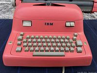 Front view of IBM electric typewriter showing red body and gray keyboard keys.