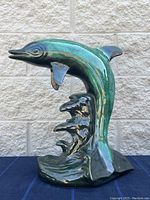 Full view of iridescent green ceramic dolphin figurine on wave base against light stone wall