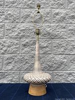 Front view of the complete Mid-Century Modern ceramic table lamp on wooden base against stone wall background.