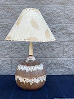 Front view of a mid-century modern table lamp showing ceramic base with brown and white glaze and handmade paper shade with leaf details.