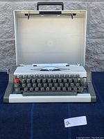 Olympia AEG Traveller De Luxe typewriter opened inside its hard carrying case showing keyboard and paper feed area.