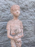 Front view of ceramic sculpture of boy holding dog with visible facial features and textured shirt, showing height and proportions.