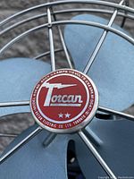 Close-up of red and white Torcan logo badge on center of fan cage showing model number and electrical specs.