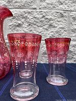Photo showing close-up of two cranberry glasses with hand-painted white and gold floral and dot details