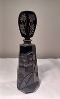 Front view of black glass scent bottle showing octagonal shape and floral carved matte glass design on bottle and stopper.