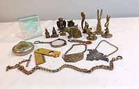 Overall group of glass block, pocket watch, razor, chains, pendants, multi-tool and brass figurines arranged on table