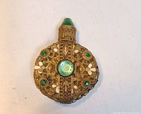 Front view of gold-coloured filigree scent bottle with green gem accents and white floral details