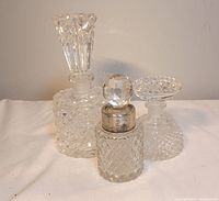 Three diamond cut crystal perfume decanters displayed upright with stoppers in place on white cloth background.