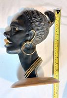 Side profile of the bronze bust sculpture showing detailed hair braids, hoop earring, necklace, and black patina with golden highlights.