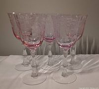 Front angle view of five pink Depression glass goblets showing etched floral designs and patterned stems.