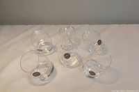Six clear egg-shaped shot glasses arranged together on a white surface showing their shape and size.