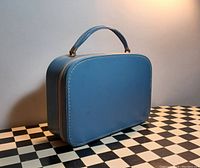 Side view of the blue rectangular hat box with stitched detail and handle.