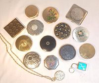 Group shot of assorted vintage compacts, perfume pendant, and key chain music box on white background