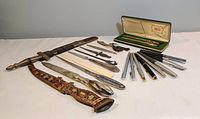 Overview of six letter openers and twelve writing instruments laid out on a white surface