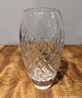 Oval-shaped crystal vase with diamond and vertical-cut patterns on wooden surface