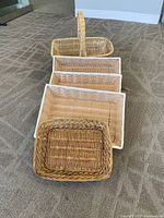 9 woven baskets arranged in a line showing different shapes and sizes, including 4 rectangular baskets with white trim and smaller baskets in natural tan colors.