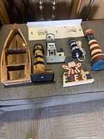 Photo showing set of Americana decor items: wooden canoe planter, three lighthouses (one electric with plug), and Freedom sign on grey surface.