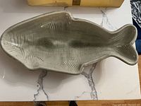 Gray pottery fish-shaped serving platter on beige surface, showing texture and scale details.