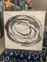 Abstract circular swirl painting in black and brown tones on light background, showing texture and brush strokes.