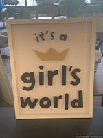 Framed art print with the phrase 'it's a girl's world' in black and gold lettering