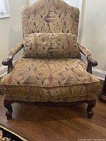 Front view of vintage upholstered armchair showing decorative patterned fabric and matching lumbar pillow.