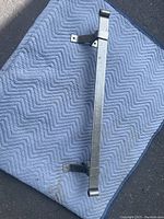 Photo shows a 48-inch long iron bar with two metal mounting brackets attached, placed on a blue textured moving blanket outdoors.
