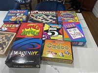 Photo of 11 kids games laid out on a table, showing colorful boxes including Monopoly Junior, Upwords, Cranium, Racko, Apples to Apples Junior, Uno, Imaginiff, Cranium Cadoo among others.