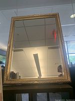 Front view of a large rectangular mirror with a gold twisted design frame, showing reflective surface and part of the surrounding room.