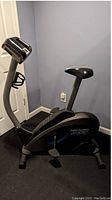 Side profile of black Pro-Form stationary bike showing adjustable seat, pedal system, and display console with built-in fan and water bottle holder.