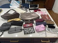 Various purses, wallets, cosmetic bags on table, some leopard print, solid colors and textured materials