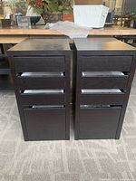 Photo showing two matching small drawer units side by side on carpeted floor, dark brown wood finish with four drawers each.