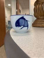 Close-up image of a single Japanese tea cup showing the fish design in blue on white ceramic.
